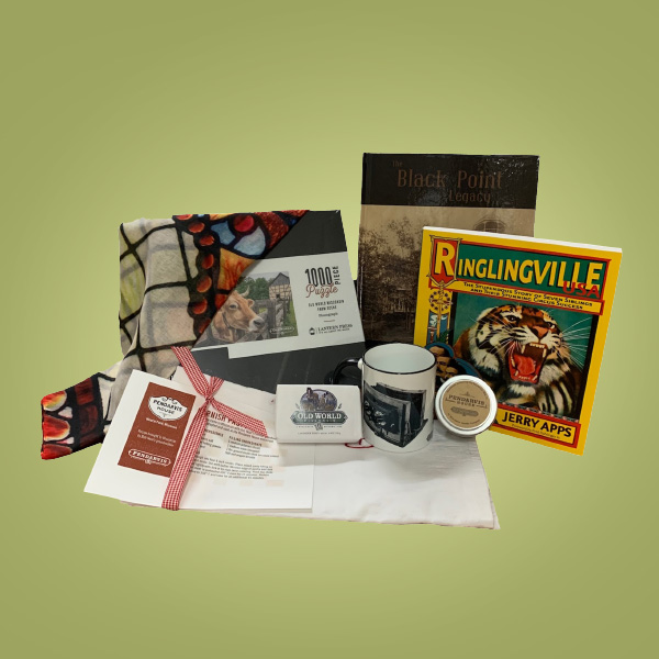 Prize Pack 3 for Member Month 2023. A Old World Cow 1000 piece puzzle, a Villa Louis stained glass sheer scarf, Old World Soap, Pendarvis tea towels featuring a cornis pasty recipe, a Pendarvis candle, Ringlingville USA book by Jerry Apps, a black and white photographed white mug, and Black Point Estate book.